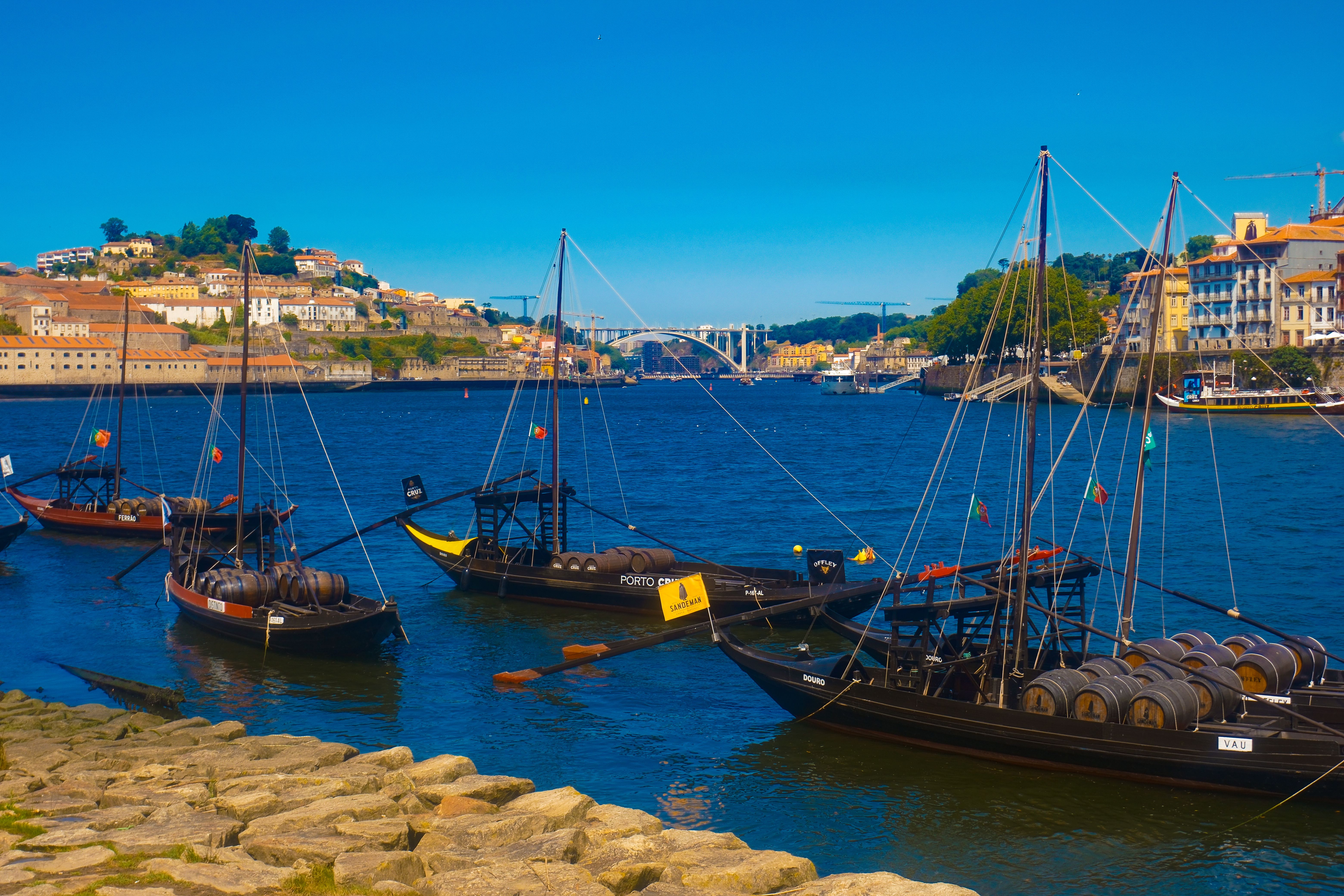 Rabelo boats on the Douro River in Porto, Portugal, transporting wine barrels under a clear blue sky.
