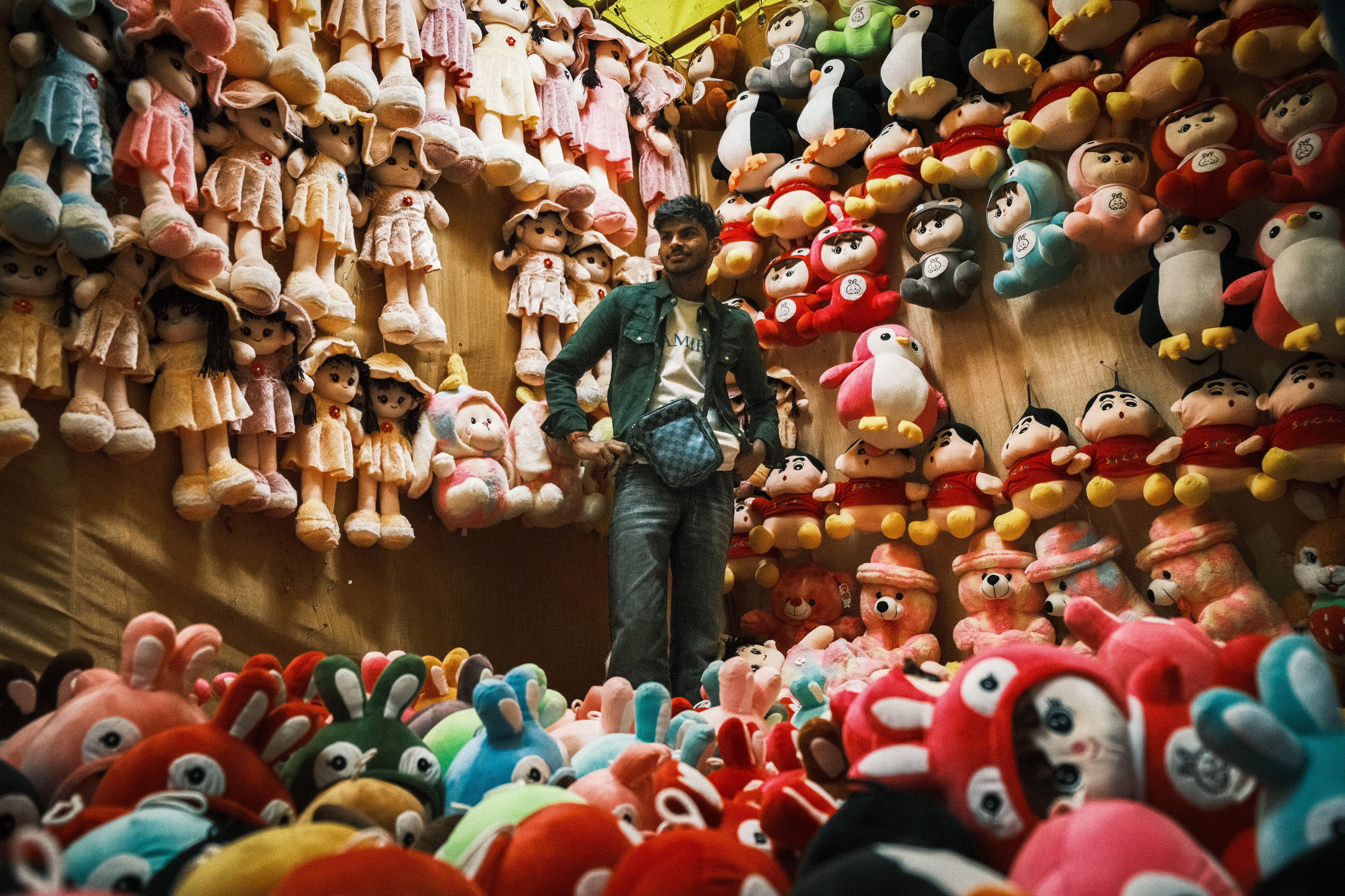 Man standing amidst vibrant plush toys at a market in Dharamshala, India.