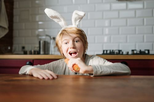 Free Child wearing bunny ears playfully eating a carrot at home. Perfect for Easter themes. Stock Photo