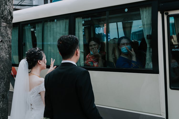 Man In Black Suit Standing Beside Woman In White Wedding Dress Waving Goodbye