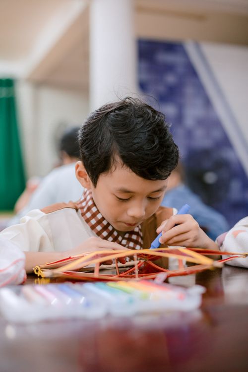 Free Young boy intensely focused on crafting project with colorful materials, showcasing creativity and concentration. Stock Photo
