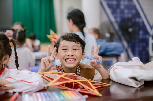 Free Smiling child holding peace sign with colorful pens and art project in classroom setting. Stock Photo
