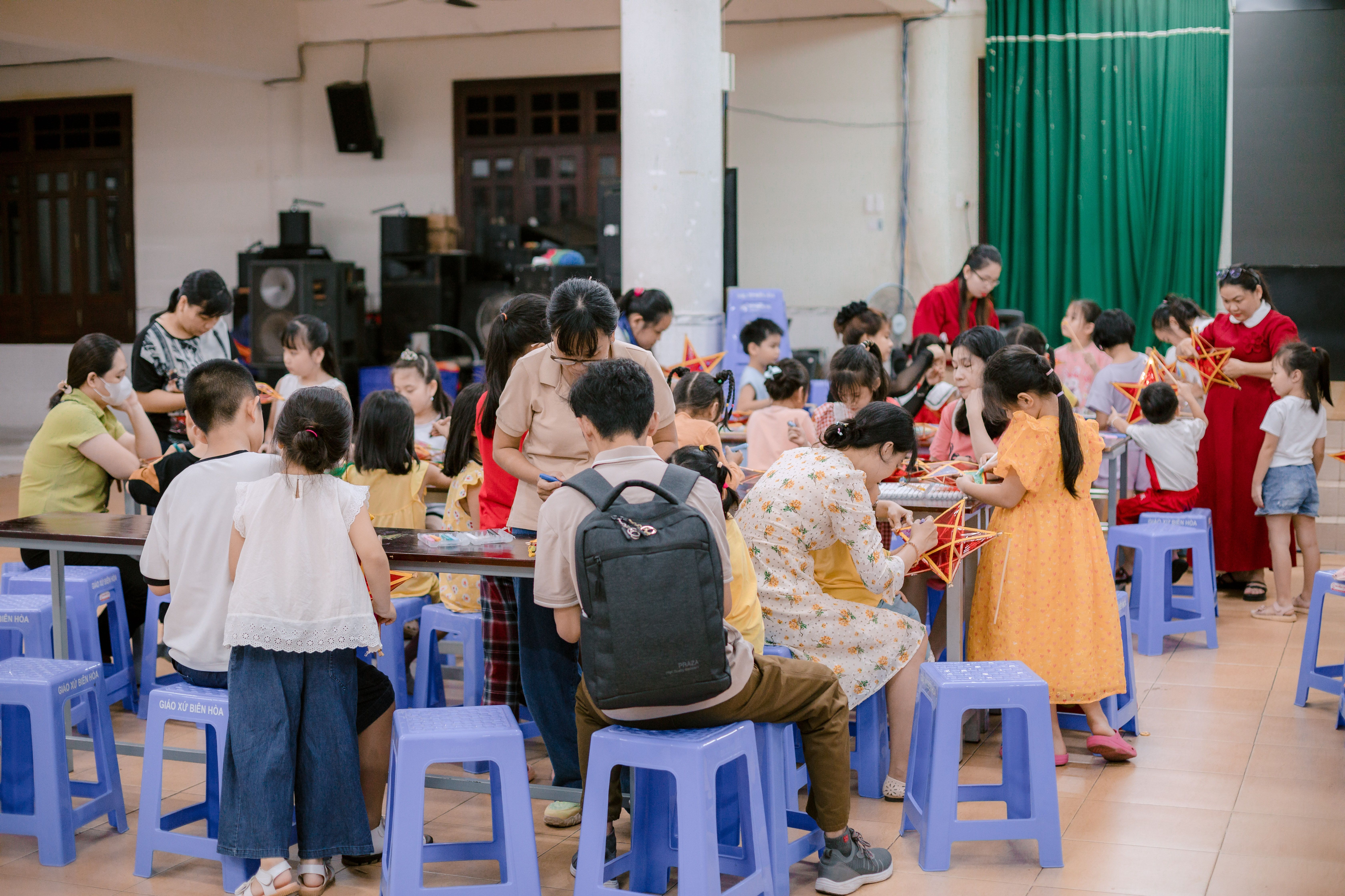 Adults and children involved in craft activities inside a community center. - Fotografer Sidoarjo