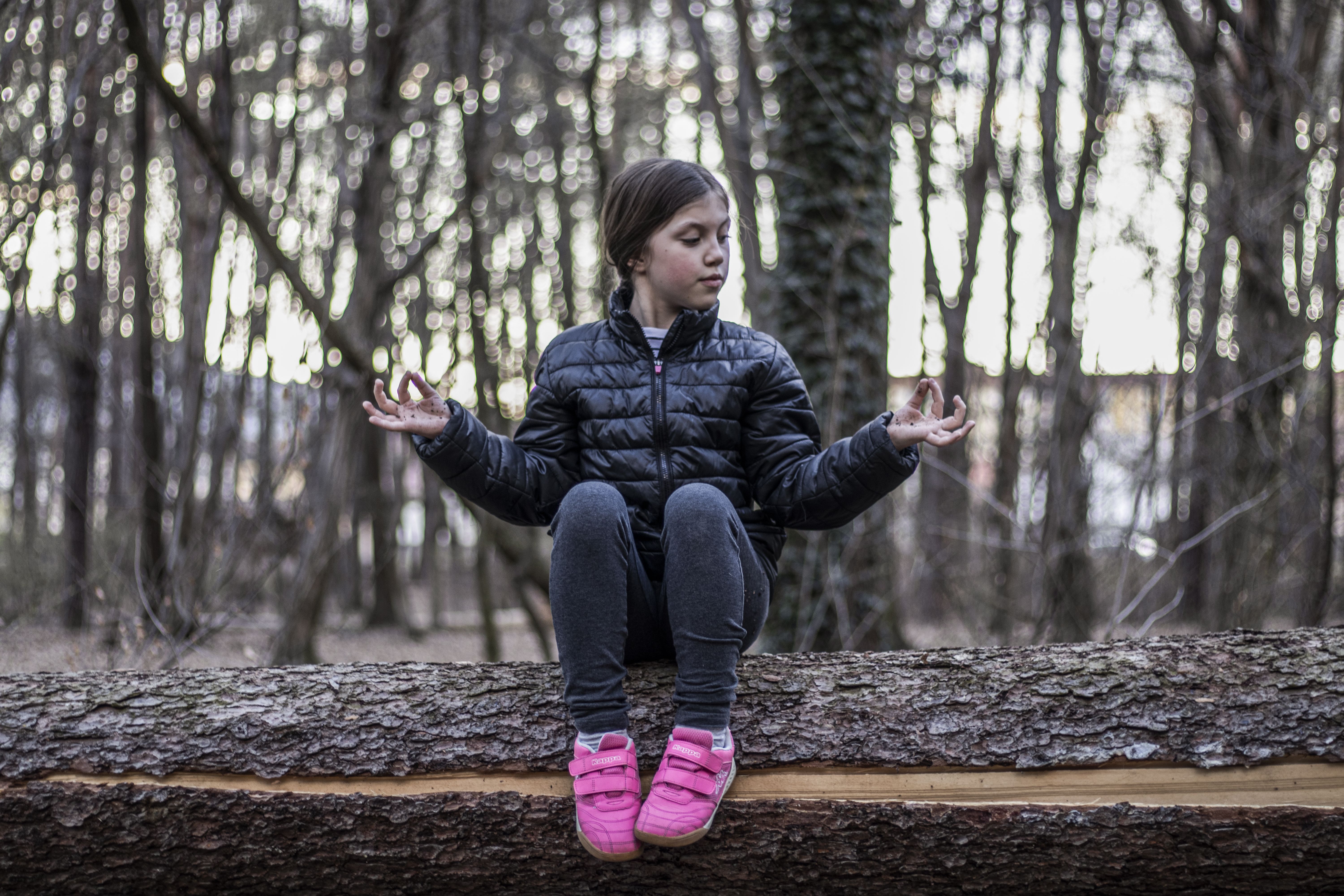 Young girl meditating on a log in a serene forest setting during daylight.