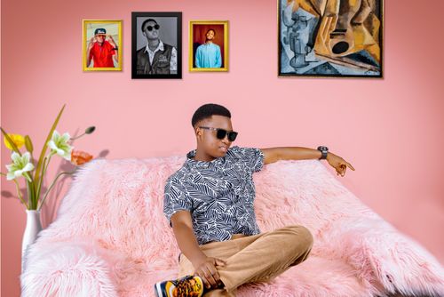 Free An adult man wearing sunglasses and a patterned shirt relaxes on a pink couch in an art-decorated room. Stock Photo