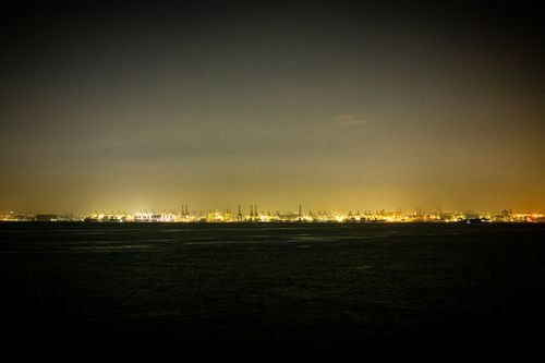Free Long-exposure nighttime view of a brightly lit harbor cityscape, showcasing industrial structures and distant city lights. Stock Photo