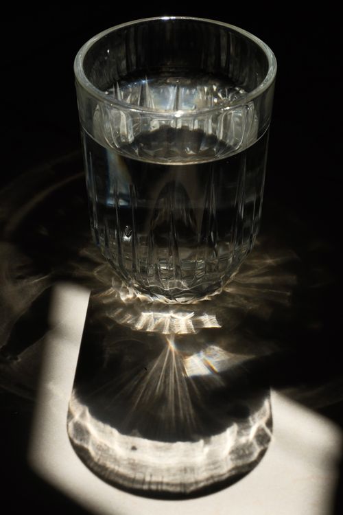 Free A glass of water casting artistic reflections and shadows. Stock Photo
