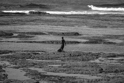 해변을 걷는 사람의 회색조 사진