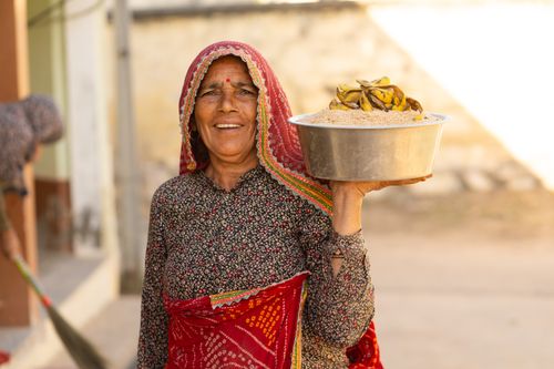 Free Smiling woman in traditional attire holds a bowl of grains and dried bananas. Stock Photo