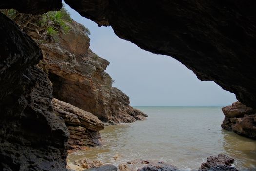Capture of a rocky cave opening revealing a serene ocean view, ideal for adventure themes.