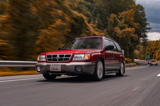 Red SUV speeding along a highway with autumn foliage and clear sky.