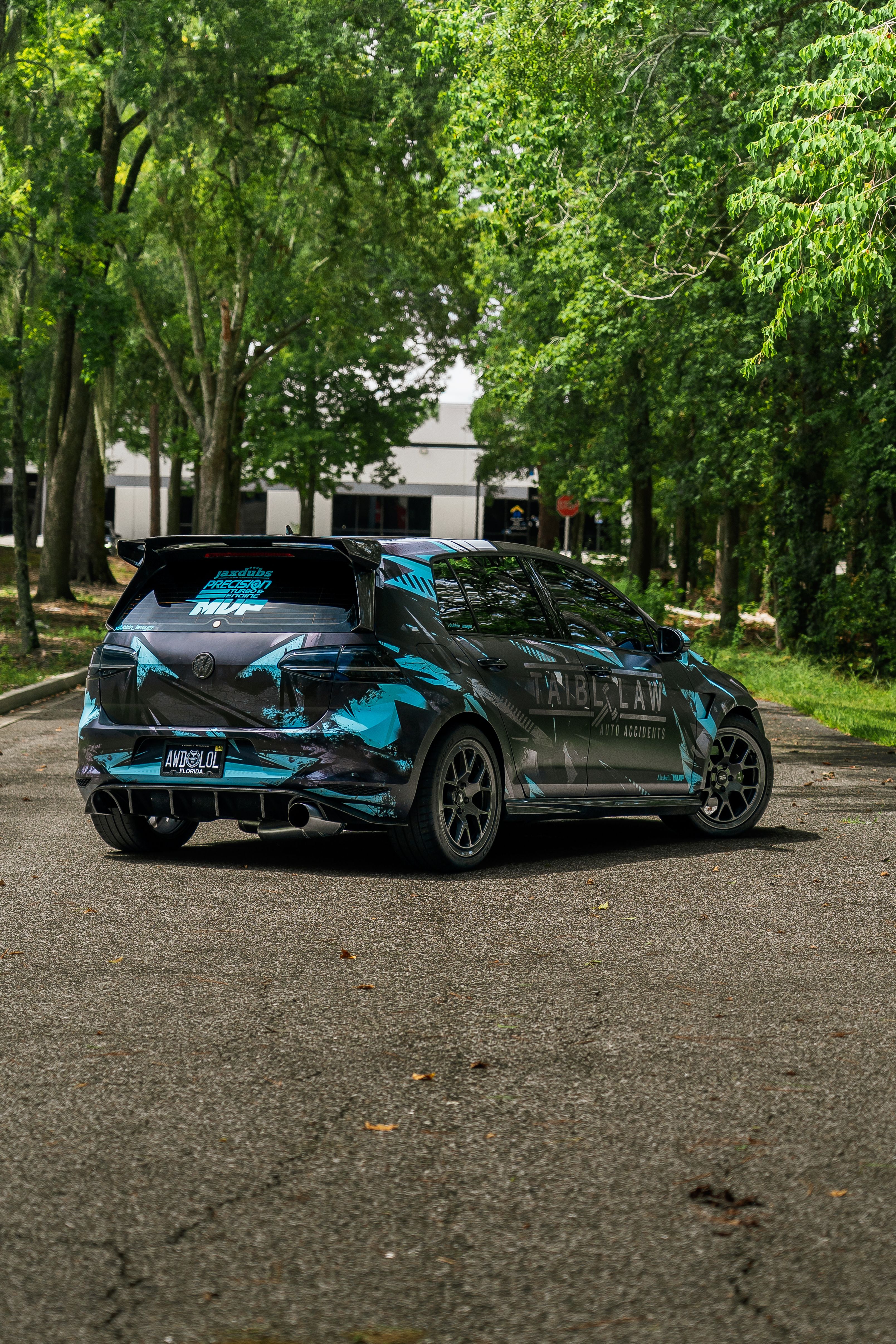 A sleek sports car with striking blue decals parked in a lush forested area.