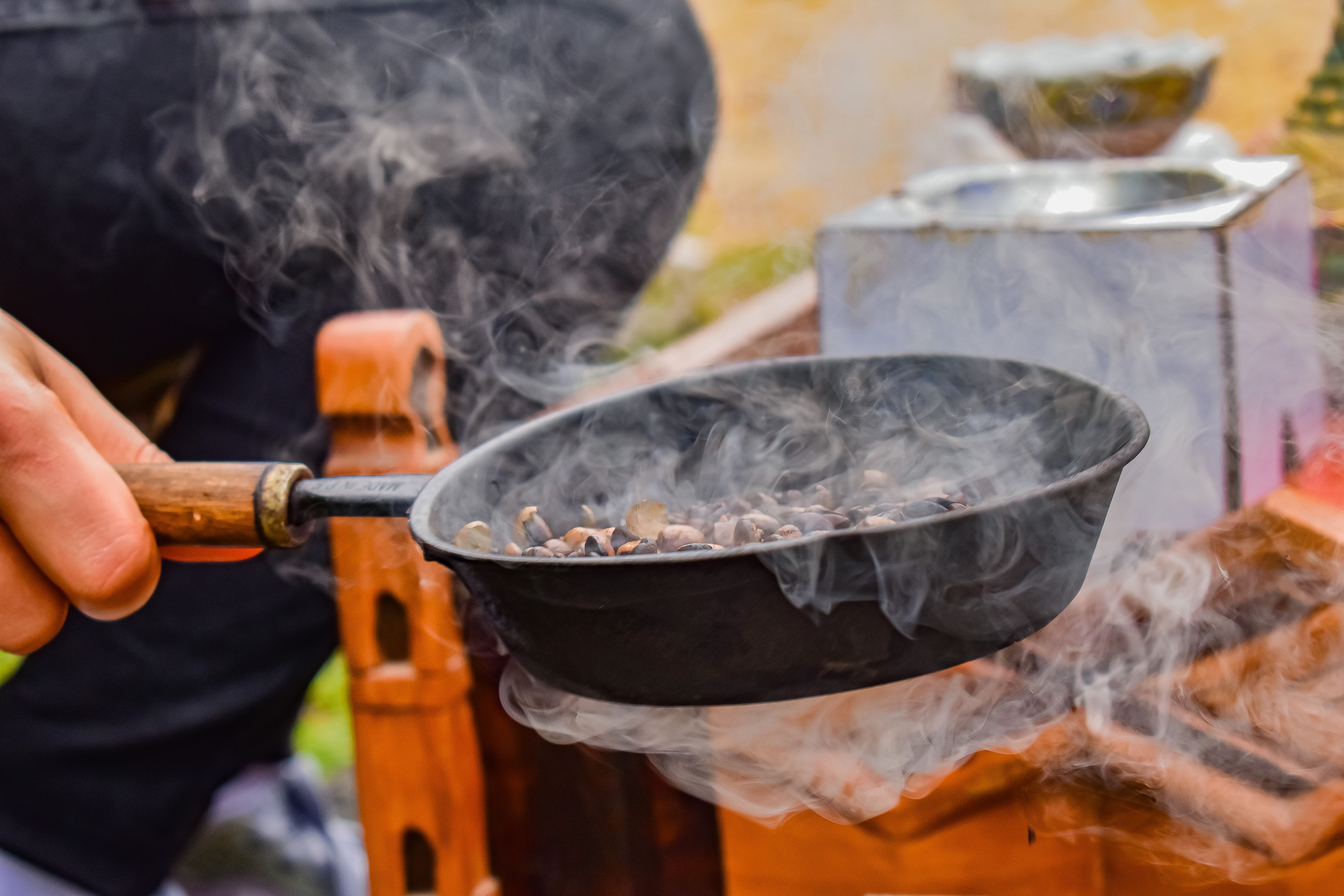 Close-up of a hand roasting coffee beans in a pan with visible smoke, capturing a traditional method.