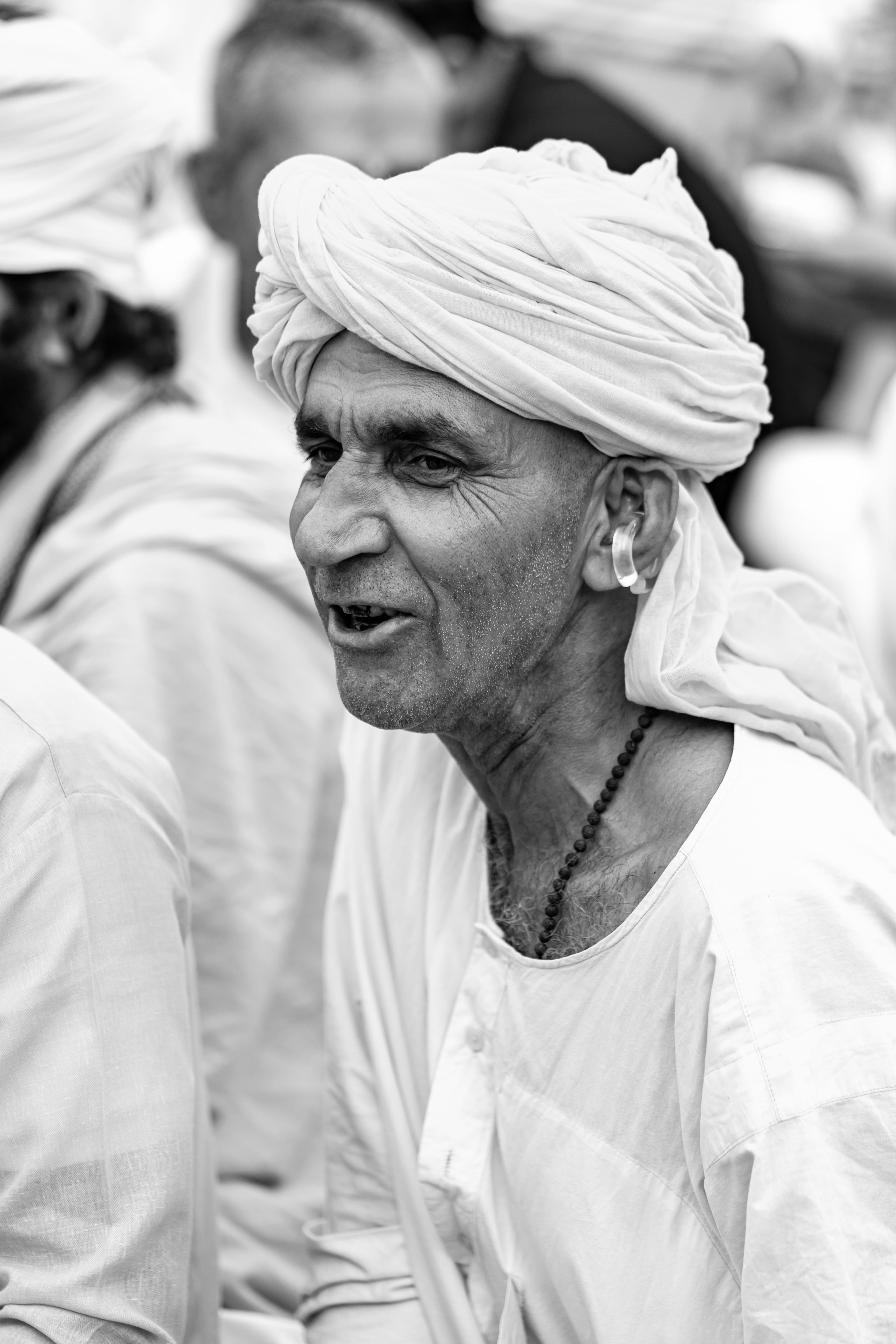 Black and white portrait of an elderly Rajasthani man wearing a traditional turban and smiling.