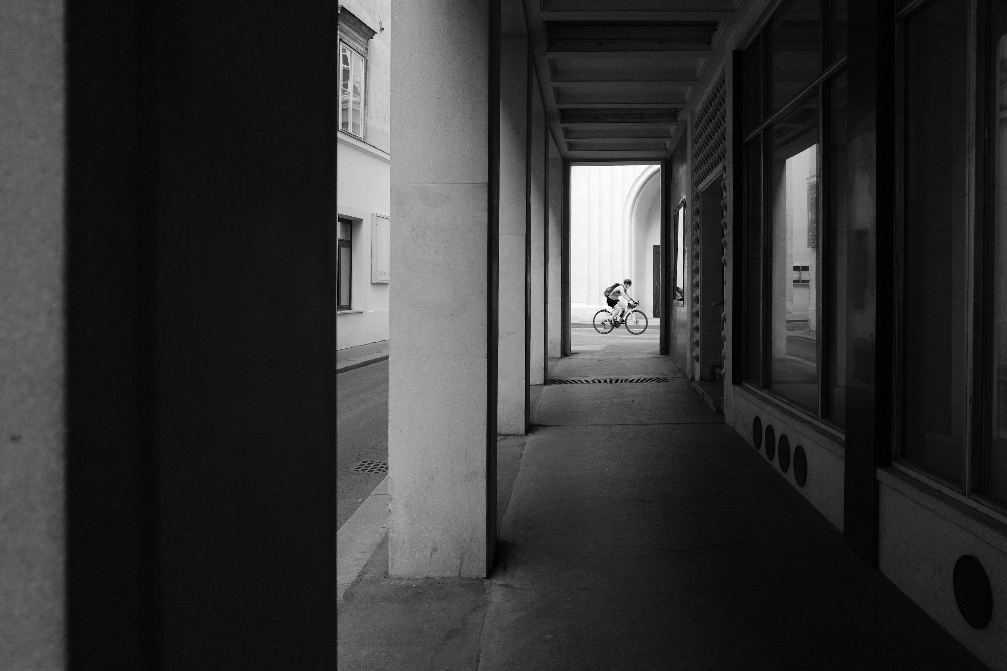 Monochrome image of a cyclist riding through an urban passageway in Vienna, Austria.