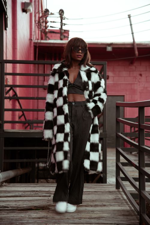 Free Stylish woman in a black and white coat poses against a red building with guardrails. Stock Photo
