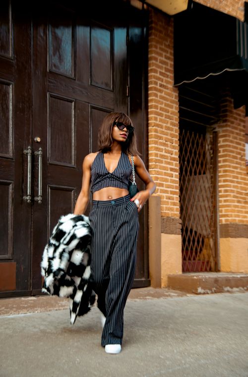 Free Fashionable woman in pinstripe suit walking near brick wall, showcasing modern street style. Stock Photo