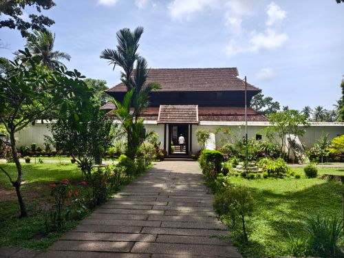 Free Beautiful traditional Kerala home surrounded by lush greenery and a well-maintained garden pathway. Stock Photo