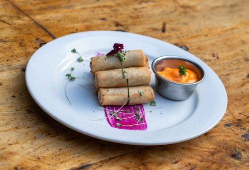 Free A plate of stacked spring rolls garnished with herbs and served with a creamy dipping sauce. Stock Photo