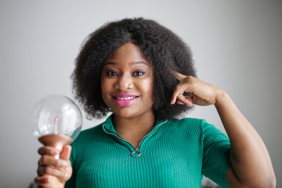 Free Positive young African American lady holding light bulb in hand on gray background Stock Photo