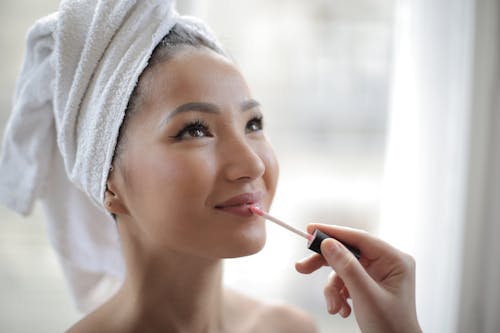 Free Beautiful young ethnic lady applying makeup on lips after shower at home Stock Photo