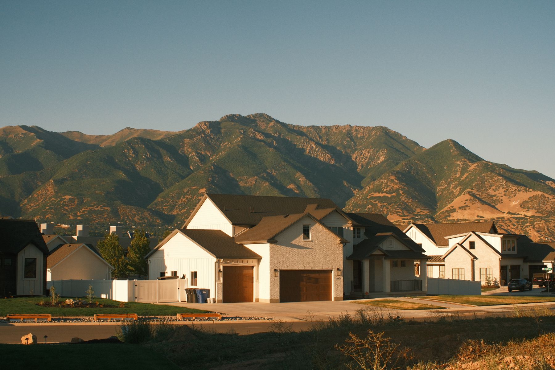 New homes with white board and batten siding at golden hour, with green foothills rising behind them