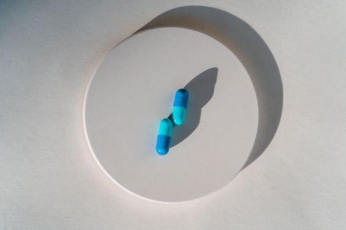 Free Two blue capsules on a round white platform in a minimalist style, casting shadows. Stock Photo