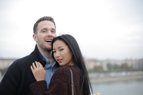 Free Positive young multiracial couple in casual warm clothes standing close to each other on street and looking at camera Stock Photo