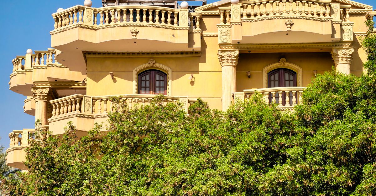 Mediterranean-style villa with ornate balconies and lush greenery under a clear blue sky.