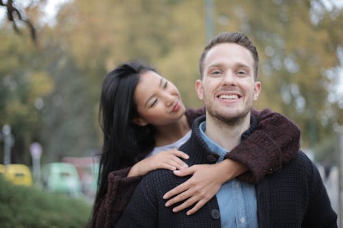 Free Positive young multiracial couple in casual warm clothes standing together in park and hugging while spending time together during romantic meeting Stock Photo