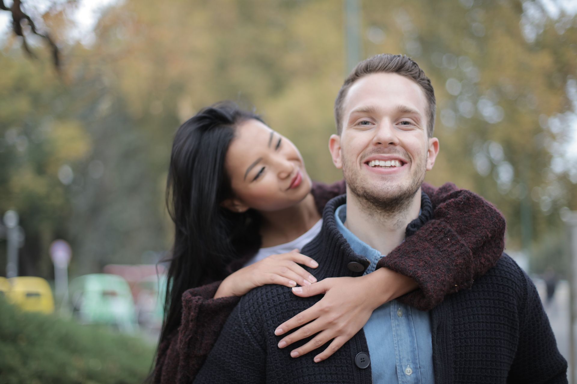Positive young multiracial couple in casual warm clothes standing together in park and hugging while spending time together during romantic meeting