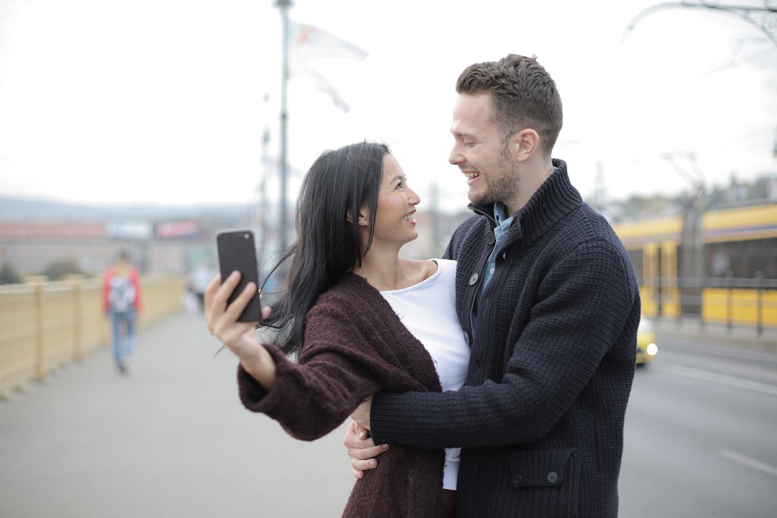 Positive young multiracial couple taking selfie while walking on street
