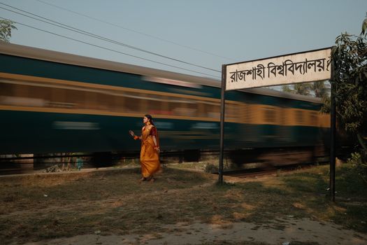 A woman in a saree walks past a moving train near Rajshahi University, Bangladesh.