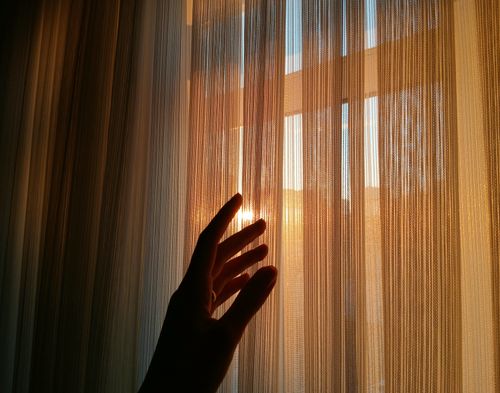 Free A hand touches translucent curtains with sunlight streaming through, creating a warm silhouette. Stock Photo