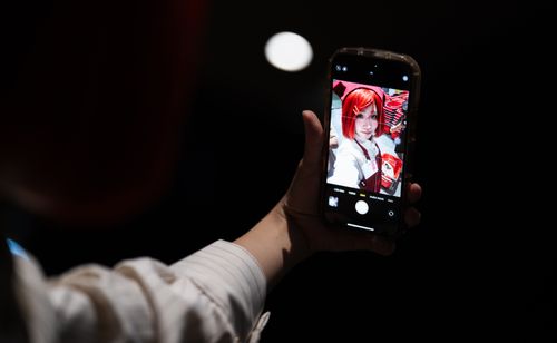 Free A hand holding a smartphone capturing a cosplayer with red hair indoors. Stock Photo