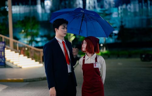 Free A businessman and an employee share an umbrella at night in an urban setting, conveying hospitality. Stock Photo