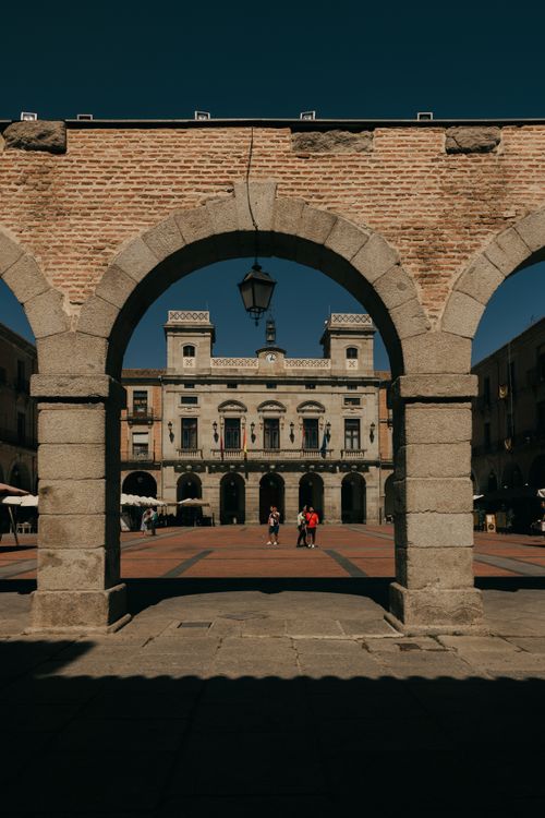 Free Charming view of a historic plaza in Ávila, Spain, framed by rustic stone arches under a clear blue sky. Stock Photo