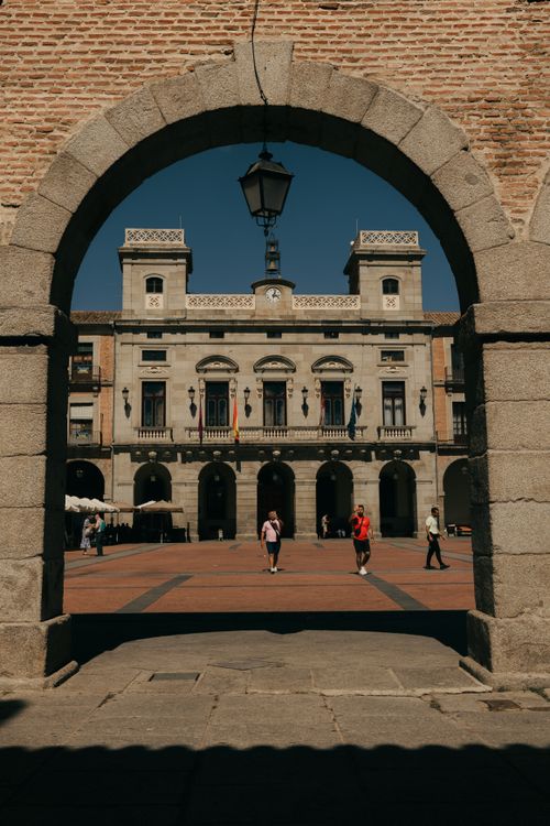 Free View of classic architecture in a plaza in Ávila, Spain through a stone archway, capturing cultural essence. Stock Photo