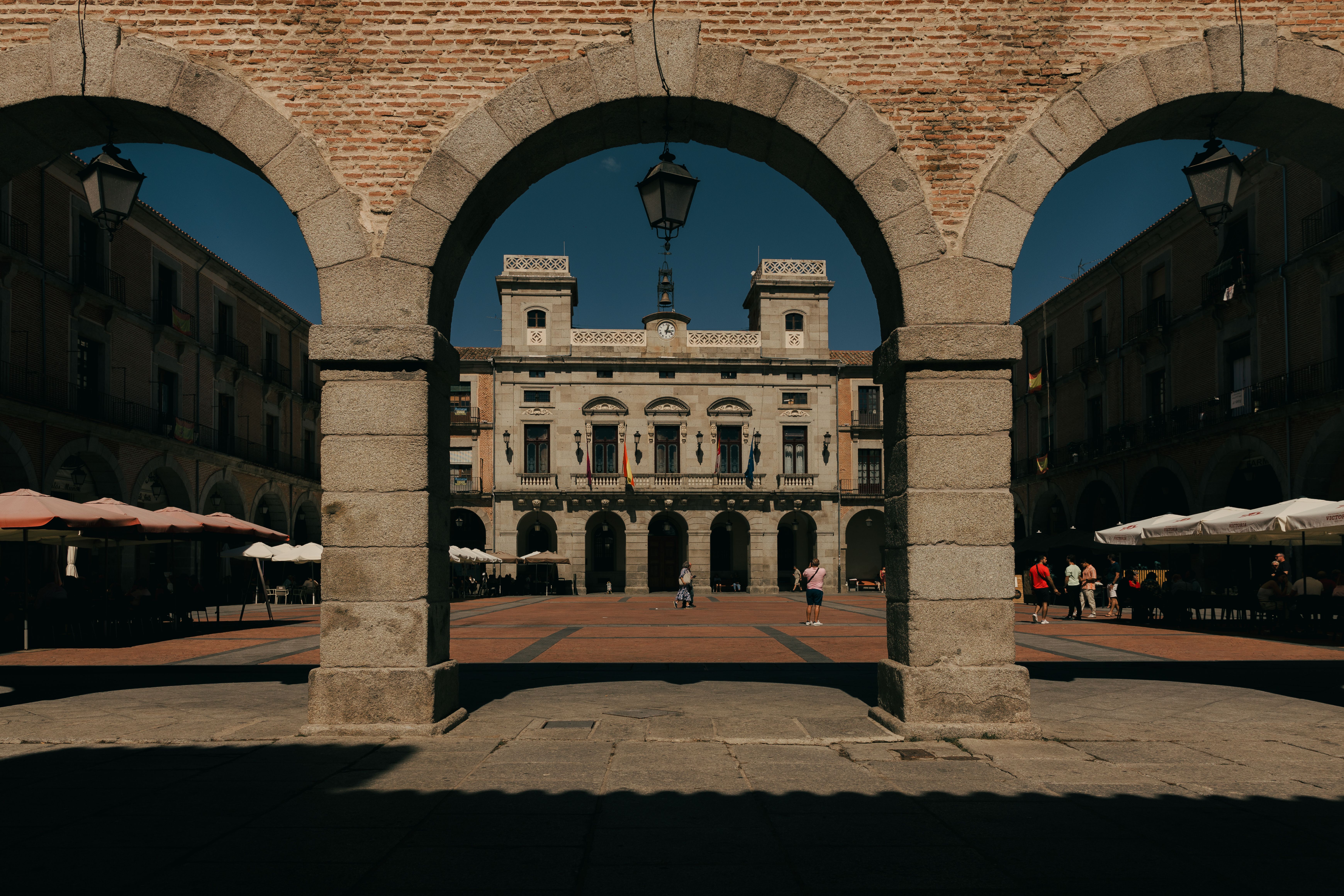 View of the historic plaza in Ávila, Spain framed by stone arches, capturing architectural beauty.