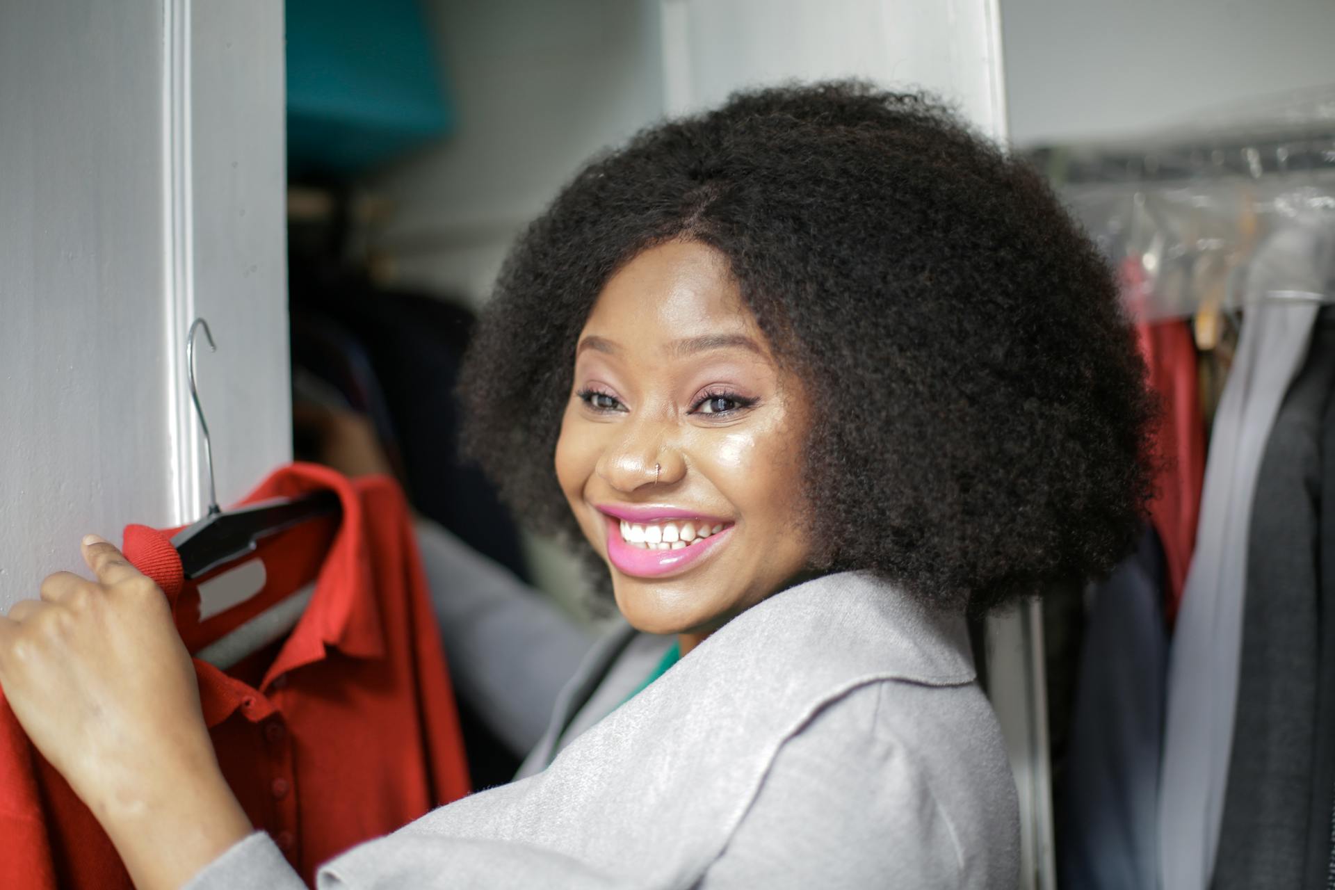 Joyful woman picking a red shirt from her wardrobe, embracing style and fashion.