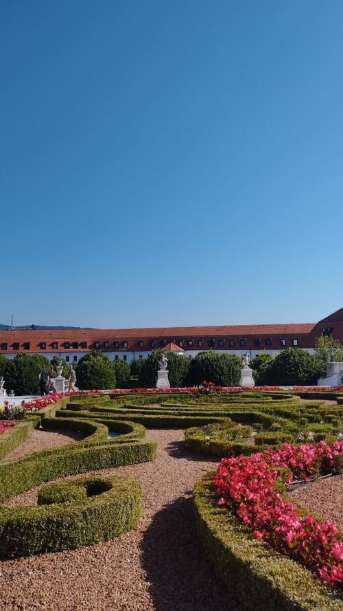 Free Beautiful ornamental garden with sculptures under clear blue sky against historical architecture. Stock Photo