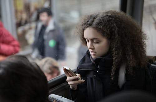 Free From above view of serious young female traveler with backpack sitting on passenger seat in bus near window and browsing smartphone Stock Photo