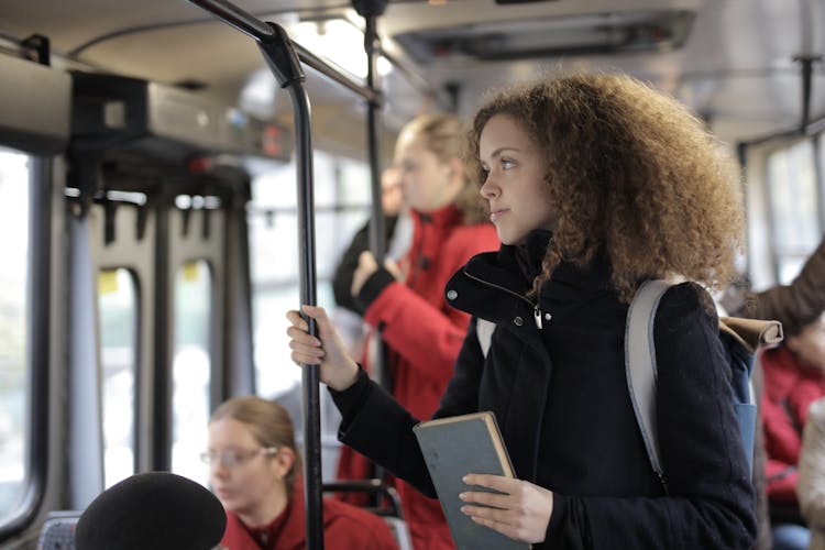 Serious Young Lady Riding Bus With Book And Backpack