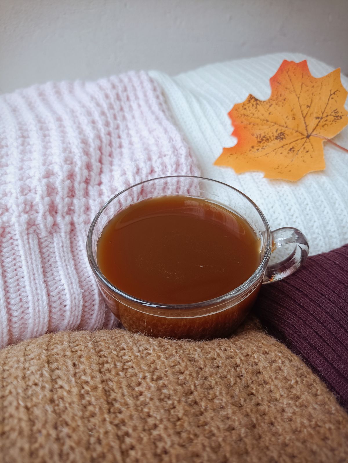 A warm cup of tea on knit blankets with a maple leaf, highlighting cozy autumn vibes.