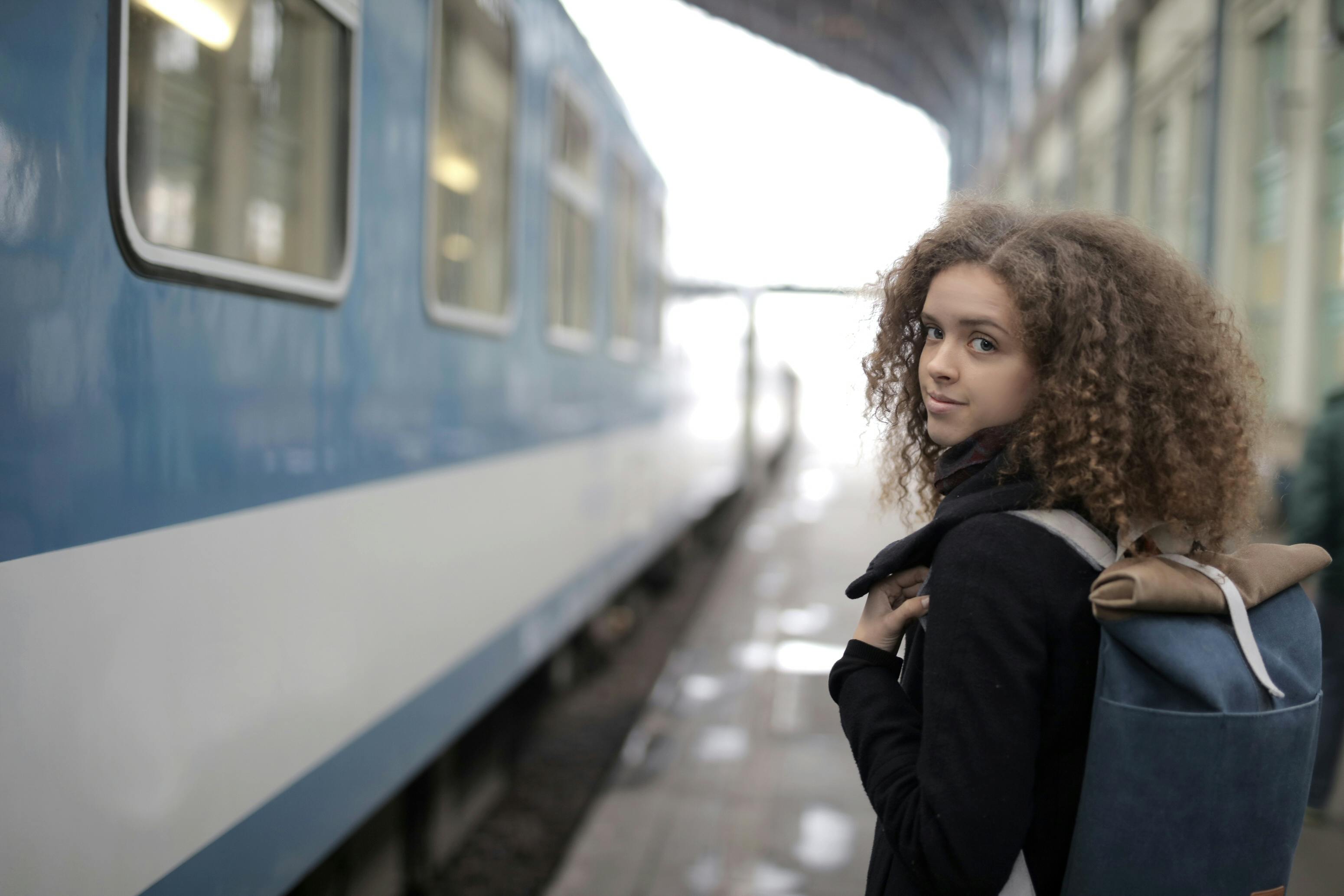 Charming young lady with backpack standing on platform near train