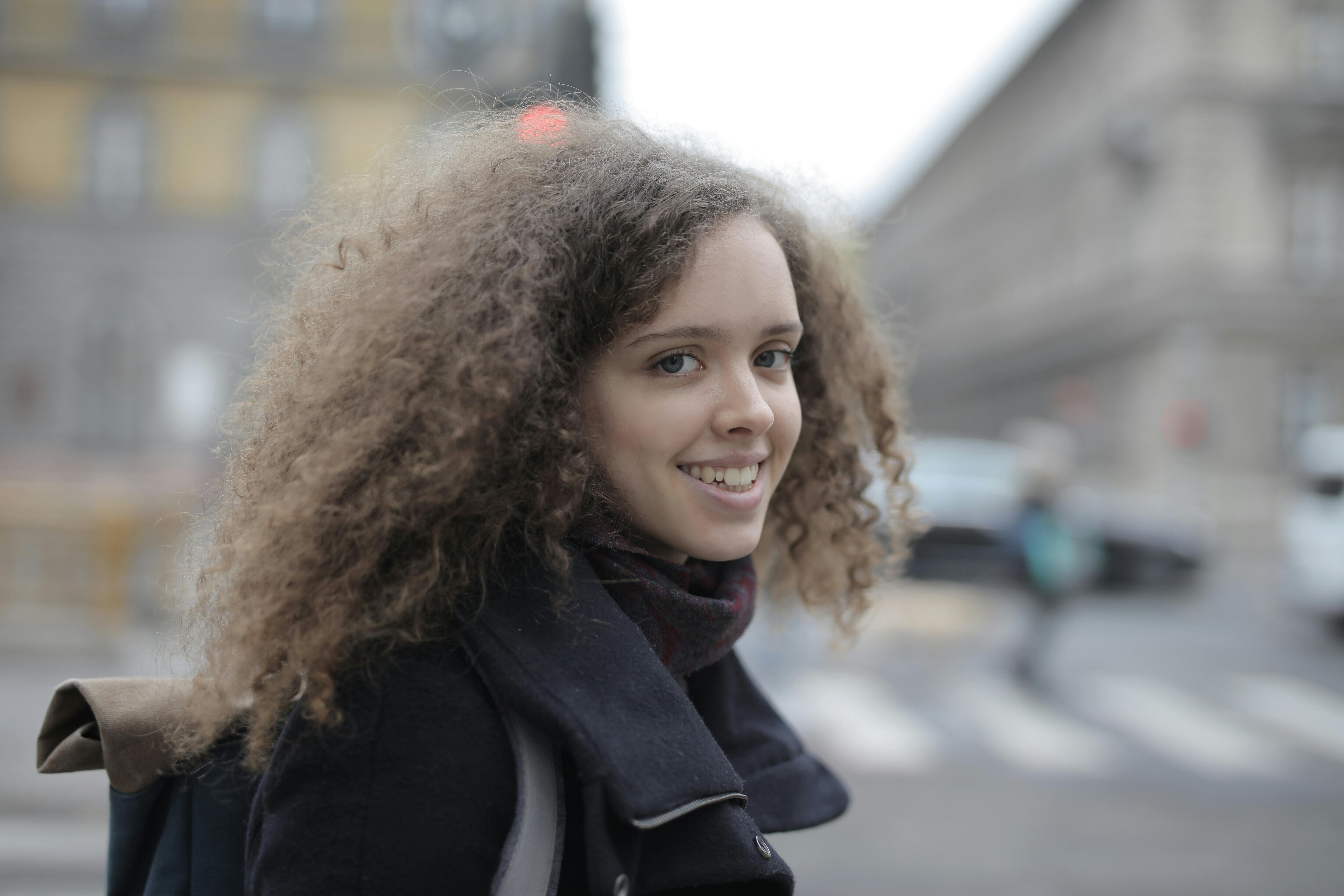 Smiling young woman with curly hair strolling through the city, embodying joy and exploration.