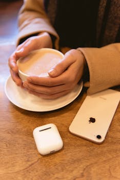 A warm coffee in hand next to a smartphone and earbuds on a wooden table, evoking relaxation.