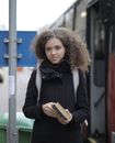 Serious young lady with book standing on bus stop on street