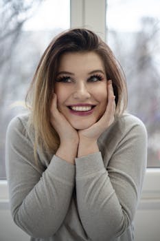 Happy woman with blond hair and bright smile posing indoors in soft light near a window.