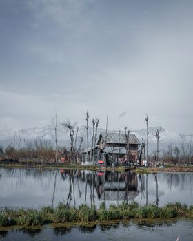 克什米尔一座坐落在反光湖边的房屋，宁静祥和，远处群山白雪皑皑